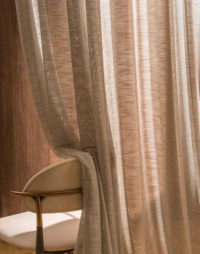 Warm solid sheer curtain tied back beside a chair